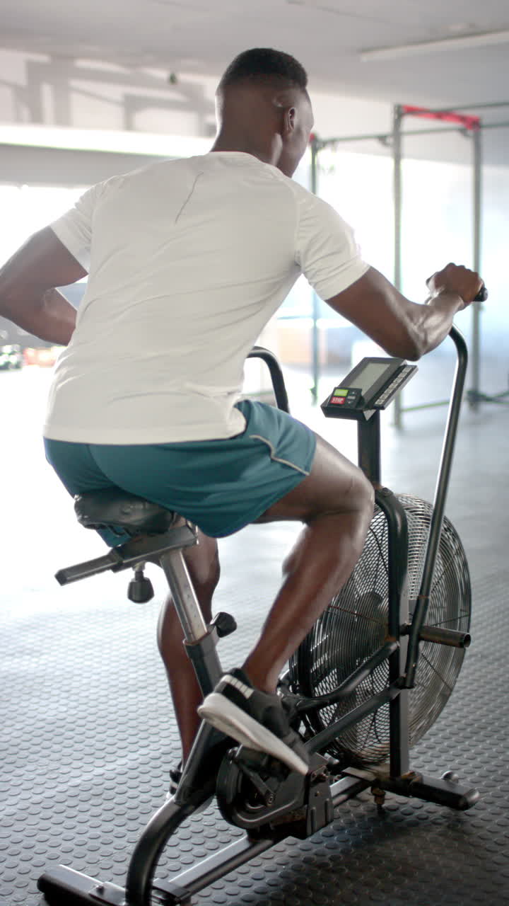 Vertical video: Exercising on stationary bike, man in gym wearing athletic clothing