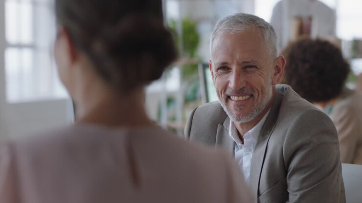 mature businessman chatting to intern discussing job interview colleagues having conversation in office enjoying teamwork