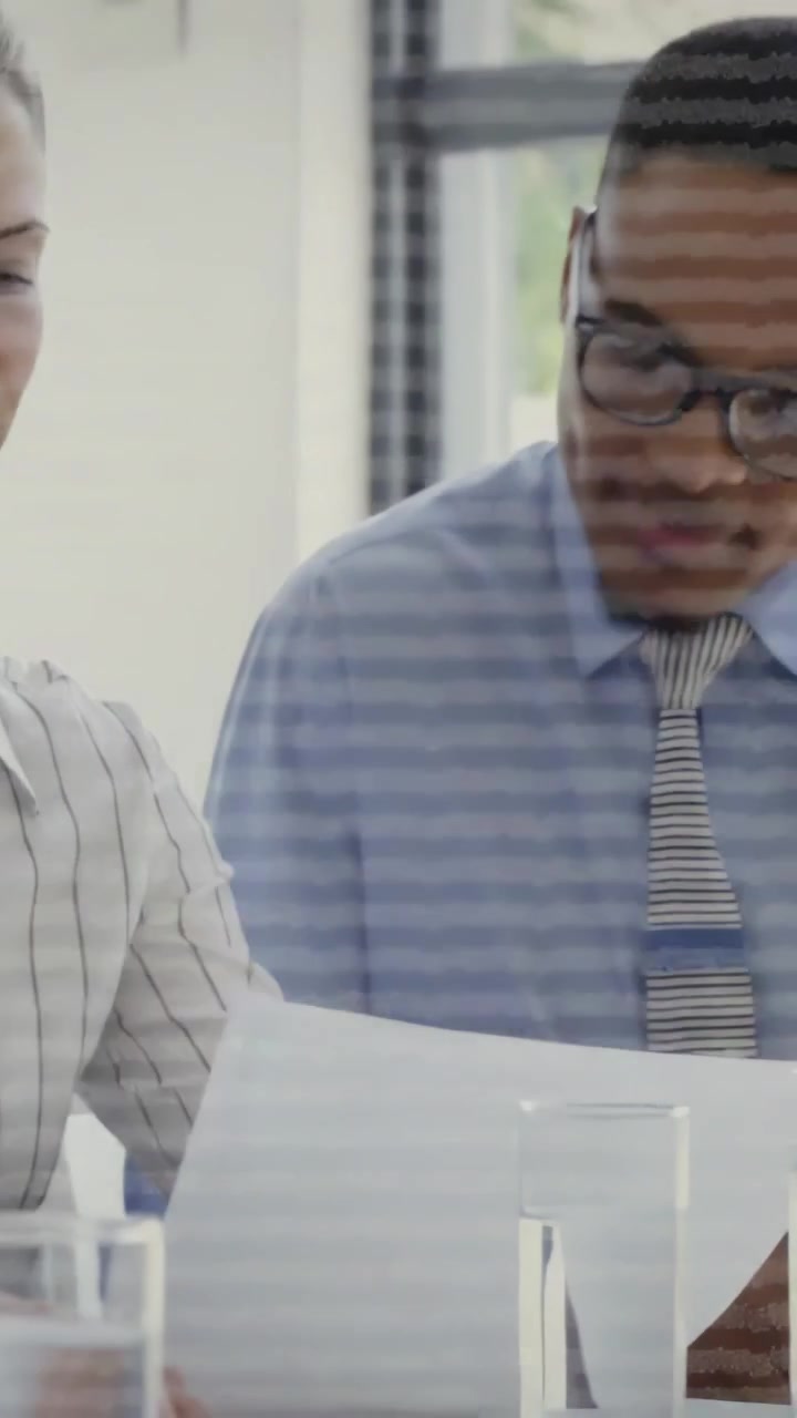 Vertical video: Team reviewing docs in office meeting with two glasses, woman turning and speaking