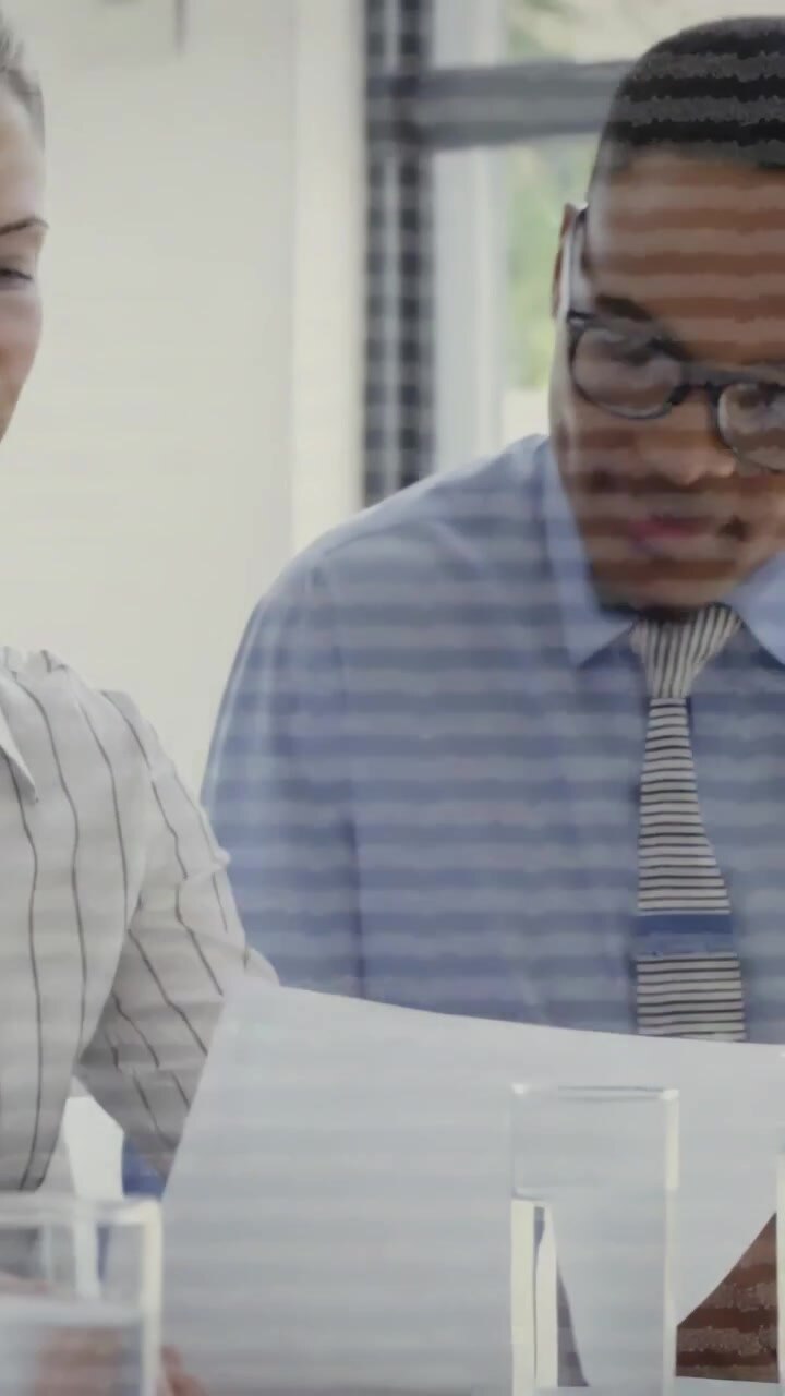 Vertical video: Team reviewing docs in office meeting with two glasses, woman turning and speaking