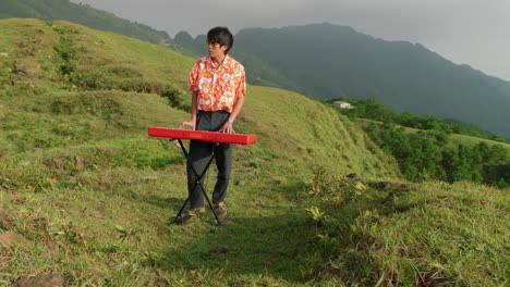 Handsome-man-playing-synthesizer-standing-on-meadow,-at-sunset