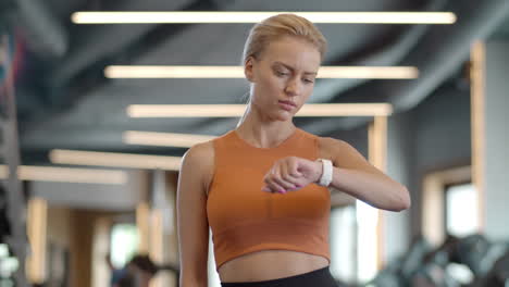 Excited-woman-looking-at-wrist-watch-at-gym.-Sportswoman-standing-in-sport-club