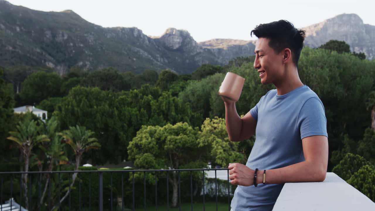 Asian man enjoying morning coffee on balcony with scenic mountain view, copy space