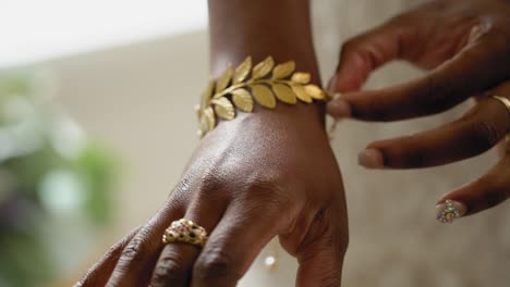 hermosa novia intentando su pulsera de hoja de oro mientras está en su vestido de novia con hermosas rosas púrpuras y blancas bokeh en el fondo