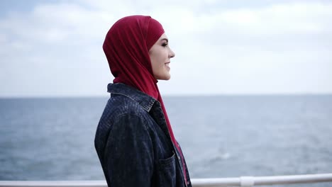 Attraktives-Junges-Mädchen-Mit-Hijab-Auf-Dem-Kopf-Geht-Angeblich-In-Der-Nähe-Des-Meeres-Spazieren,-Mit-Fliegenden-Möwen-Im-Hintergrund
