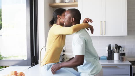 Una-Joven-Pareja-Afroamericana-Comparte-Un-Cálido-Abrazo,-Abrazándose-En-Una-Cocina-Luminosa