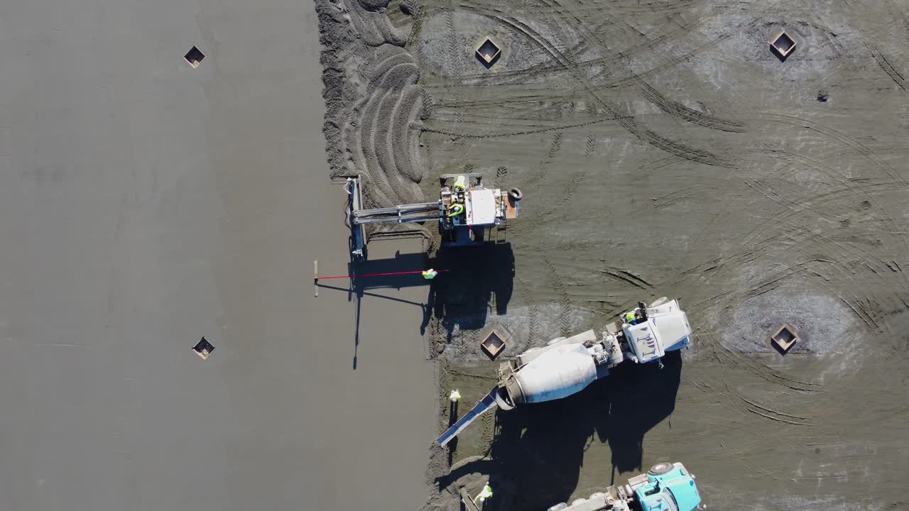 Un'inquadratura dall'alto di una betoniera, di una staggia vibrante e di operatori con lisciatrici al lavoro in un cantiere.