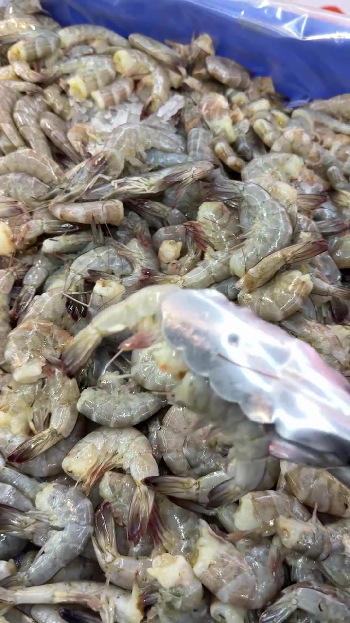 Hand Using Tongs to Select Fresh Raw Shrimp from Ice