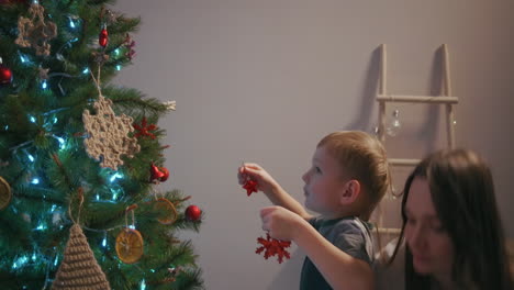mom and her son hang christmas tree toys on top of christmas tree. high quality 4k footage