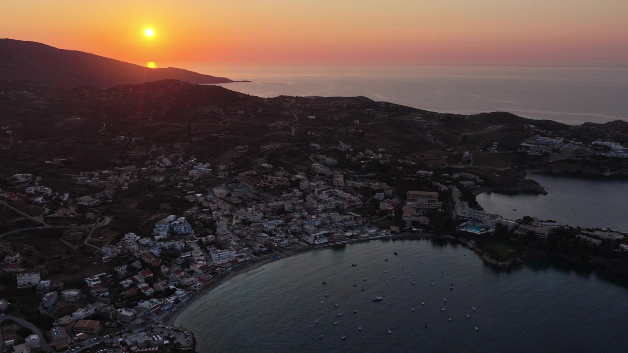 Vista aerea con drone di un tramonto rosa tenue sul mare e di una località turistica che si estende attorno alla sua baia, Agia Pelagia, Grecia