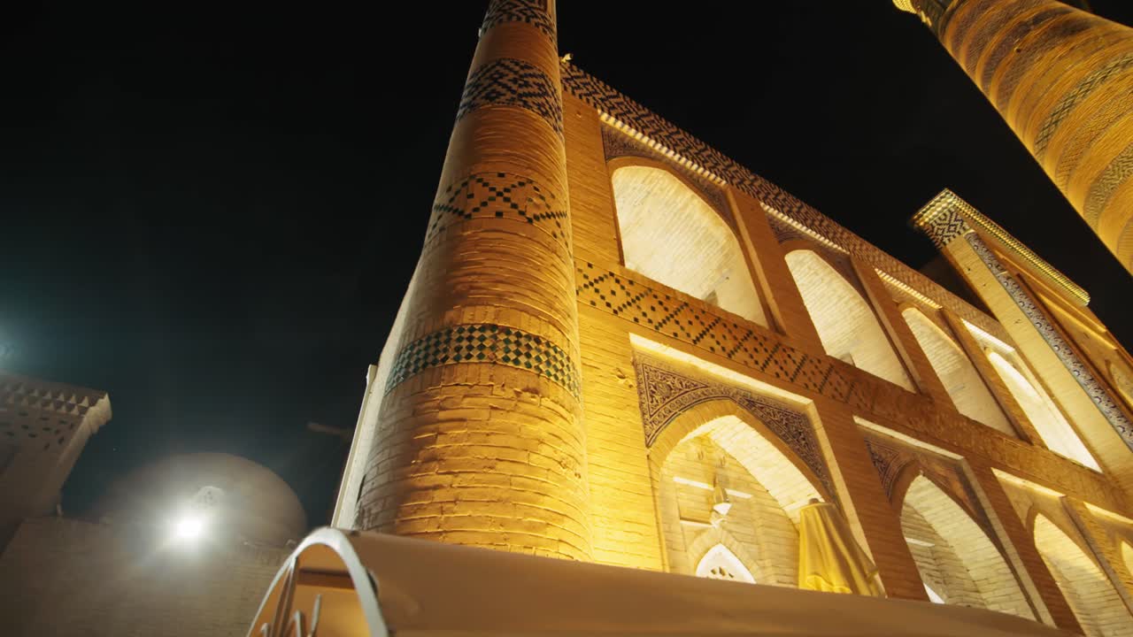 Khiva night minaret, madrasah mosque illuminated, old city in the evening. Uzbekistan silk road at night
