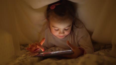 niño leyendo en la tableta bajo la manta
