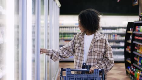 mujer de compras con carrito, abra la puerta del refrigerador en el supermercado