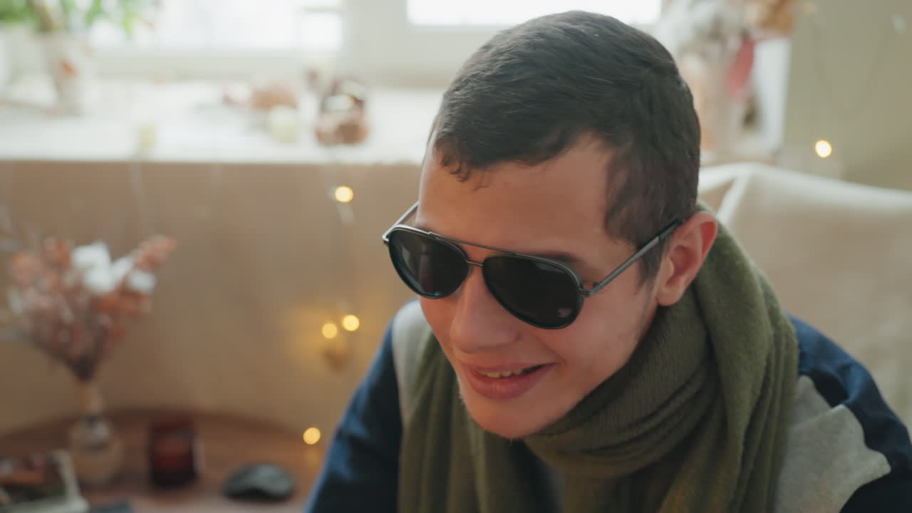 Smiling man wearing sunglasses, warm lights in cozy living room with bokeh, relaxed charm and confident vibe, subtle retro film grain and apartment decor conveying creative personality
