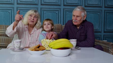 Abuelo-Y-Abuela-Mayores-Felices-Riendo,-Comiendo-Palomitas-De-Maíz,-Viendo-Películas-De-Dibujos-Animados-En-Casa