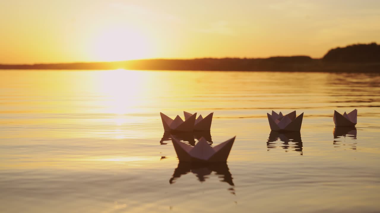 Several white paper boats on water at sunset. Paper ships in water. Origami.