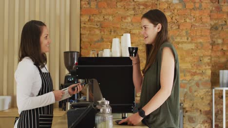 caucasian waitress receiving contactless payment and giving coffee cup to caucasian female customer