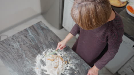 aerial view of person kneading dough on floured tiled table in kitchen, hands work on soft, sticky dough as flour spreads across countertop, traditional homemade baking process