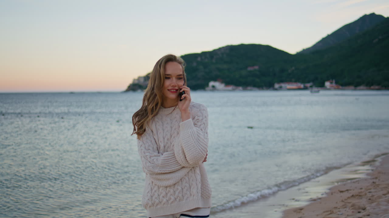 Cheerful tourist talking mobile phone standing at ocean waves on sunset closeup