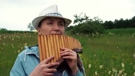 a young woman with a hat plays the pan flute in nature