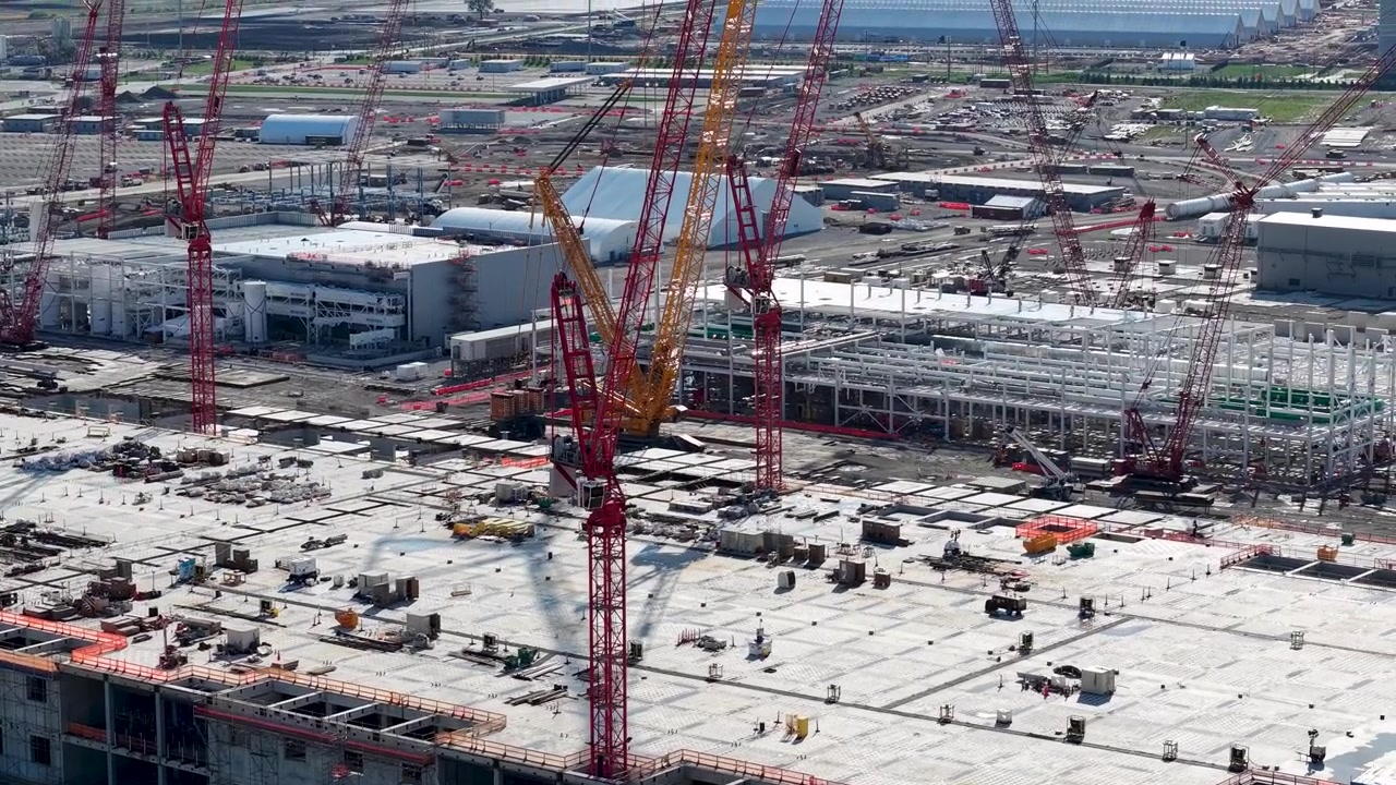 大規模な建設現場で、コンクリート製建物のデッキ上空で作業するクレーンの空撮クローズアップ