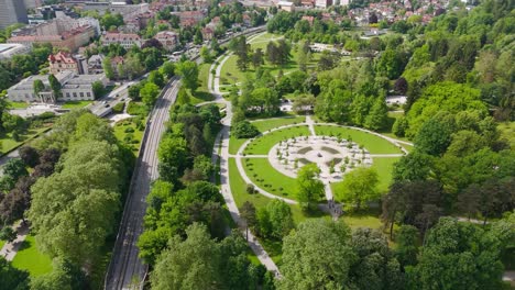 neat tivoli town park in center of ljubljana city. aerial tilt up shot. sunny day in spring season with green trees. traffic on main street. wide shot.