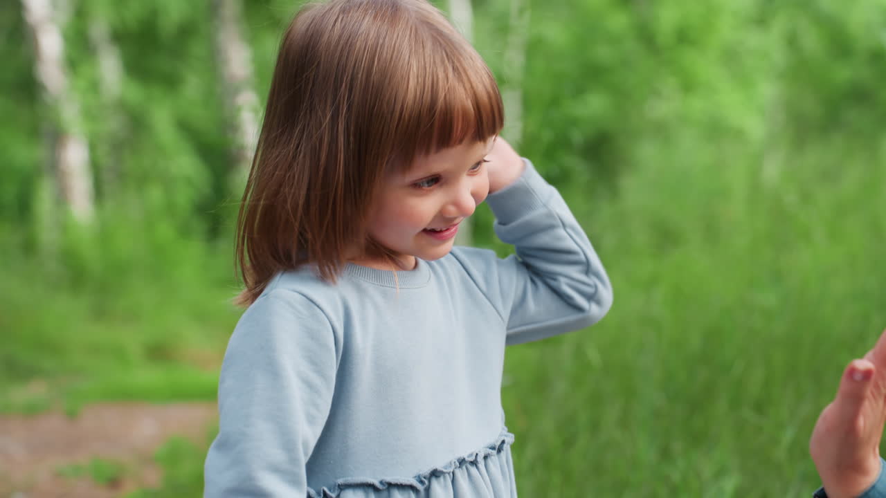Un niño pequeño adorable sonríe alegremente mientras choca las manos con su hermana y su madre durante un divertido juego al aire libre en un bosque verde, expresando amor, conexión y alegría a través de la risa.