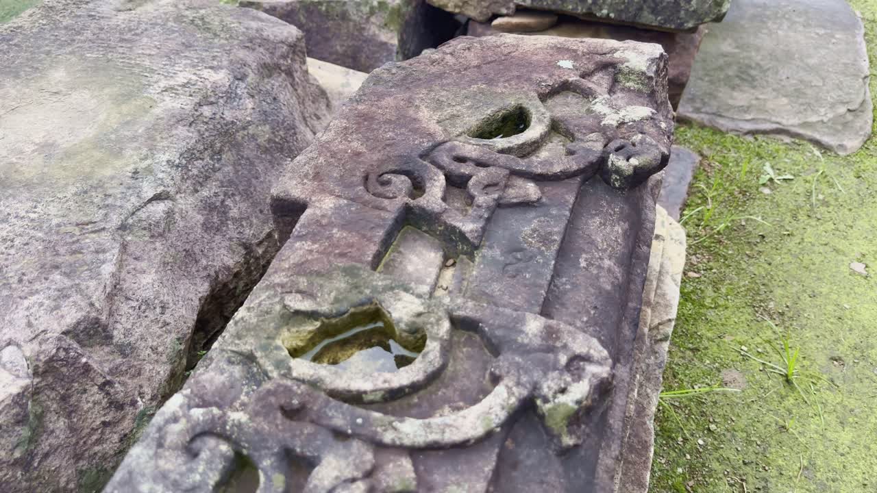 A slow push-in shot focuses on an ancient ornamental stone block, its moss-covered surface and fading carvings revealing traces of artistry that once decorated gateways or railings