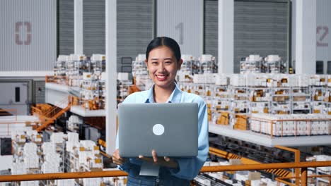 una mujer de negocios asiática usando una computadora portátil y sonriendo a la cámara en el almacén