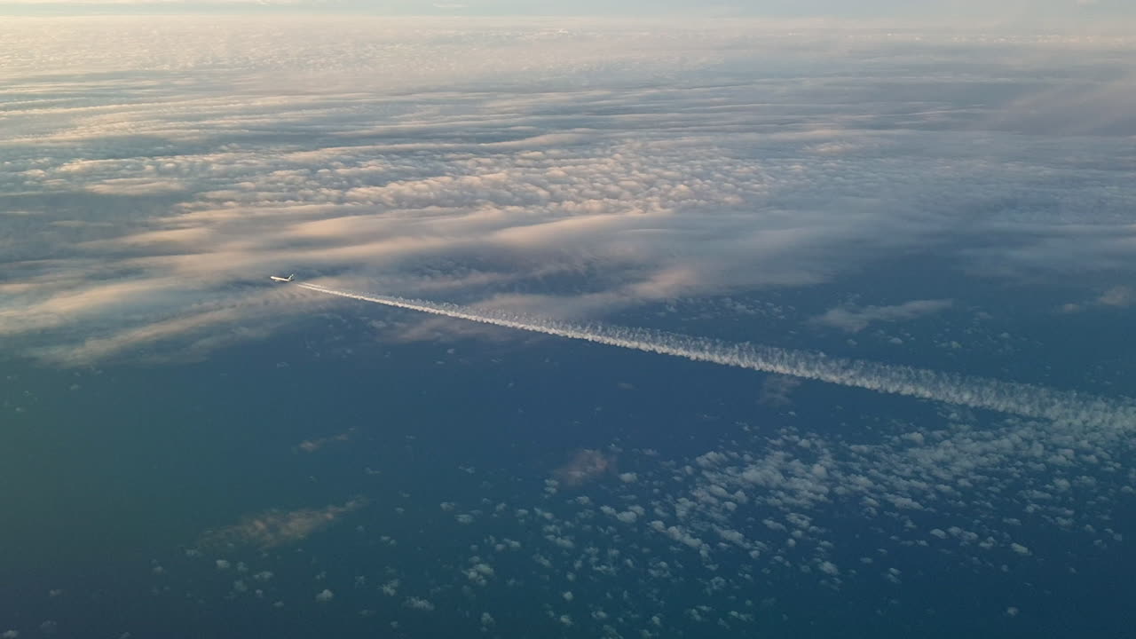 Incredible view from the cockpit of an airplane flying high above the clouds leaving a long white condensation vapour air trail in the blue sky