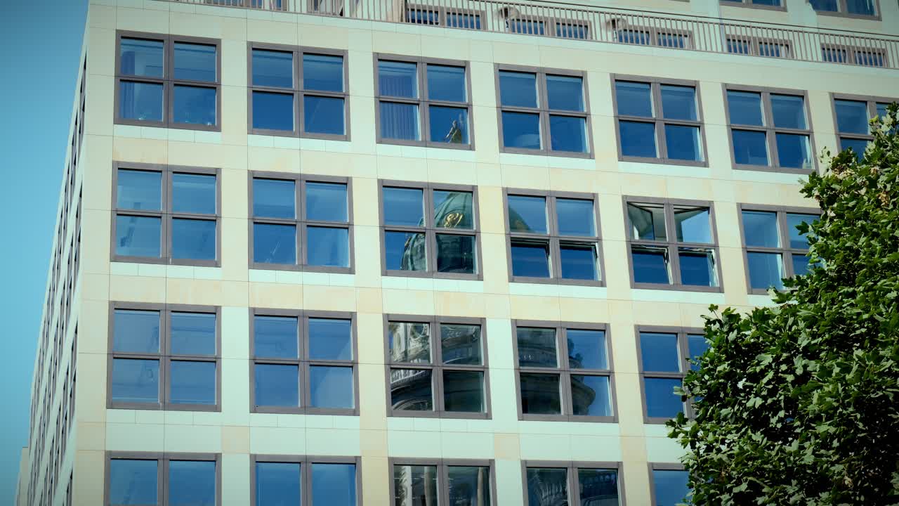 Moderna facciata di uffici con finestre ripetute che riflettono il cielo e l'ambiente urbano circostante, Berlino, Germania