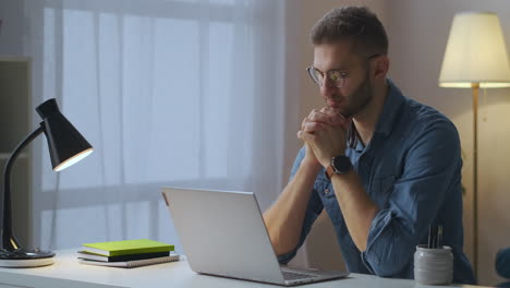 Ein-Erwachsener-Mann-Sieht-Sich-Zu-Hause-Ein-Lernvideo-Auf-Dem-Bildschirm-Eines-Notebooks-An,-Das-Sich-Per-Internet-Weiterbildet.-Porträt-Eines-Mannes-Mit-Brille-Am-Tisch-Im-Zimmer