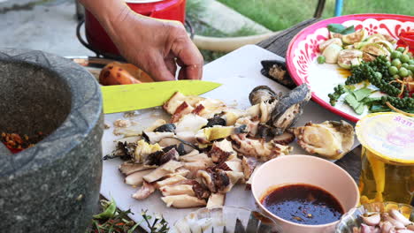 Hands-slice-cooked-sea-snail-meat-on-chopping-board