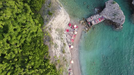 Sun-loungers-and-parasols-on-idyllic-coastline-below-cliffs,-Sveti-Nikola