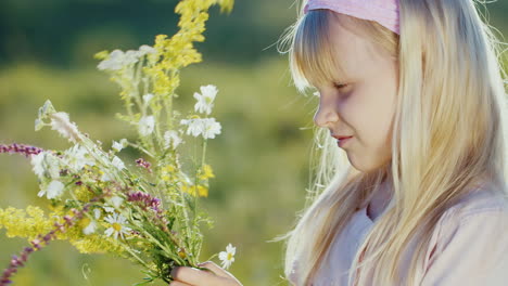 cute little girl collects composition from wild flowers on a background of green landscape