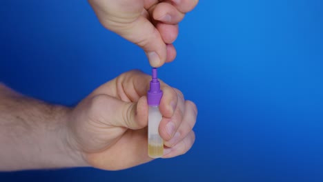 Male-breaks-off-tip-from-lid-of-dropper-bottle-filled-with-urine-for-self-testing