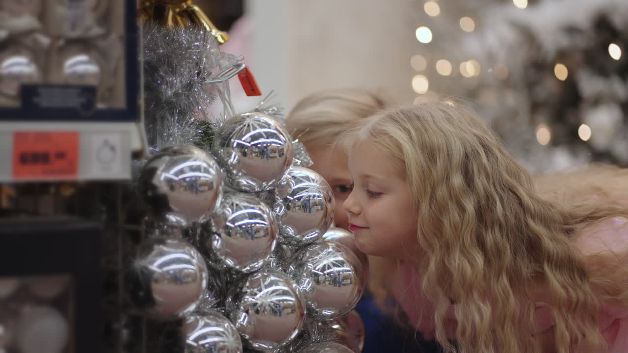 los niños se deleitan en la tienda y hacen muecas y se ríen mirando las bolas navideñas.