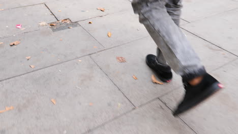 Urban-stroll-in-London,-male-with-black-sneakers,-grey-pants-slowly-walking-amidst-autumn-leaves