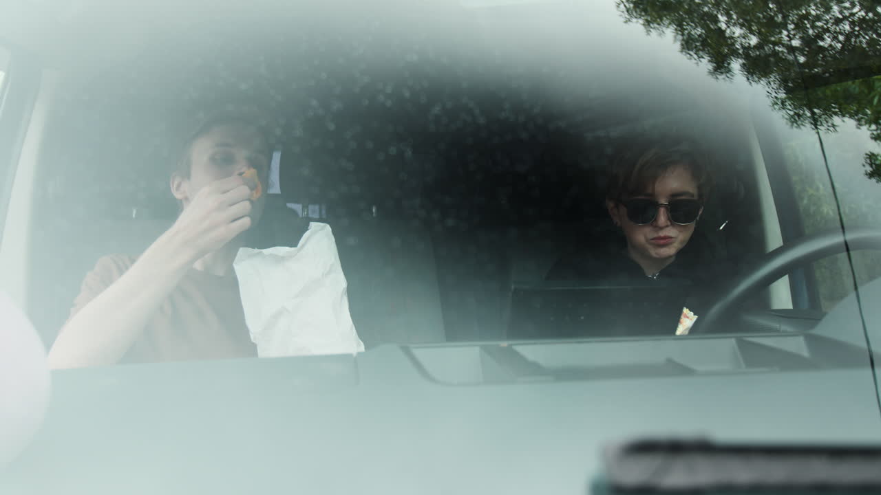 두 친구가 밴 안에서 먹고 있다