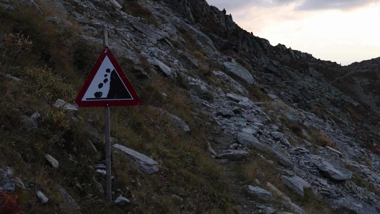 Dangerous mountain crossing across rockfall avalanche area, falling rocks sign