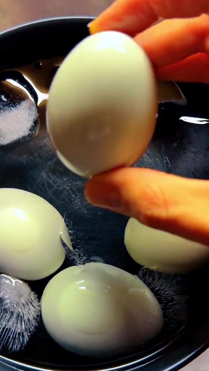 Hard boiled eggs cooling in black bowl with ice water. Close up of boiled eggs in a dark bowl with ice cubes and water for cooling process.
