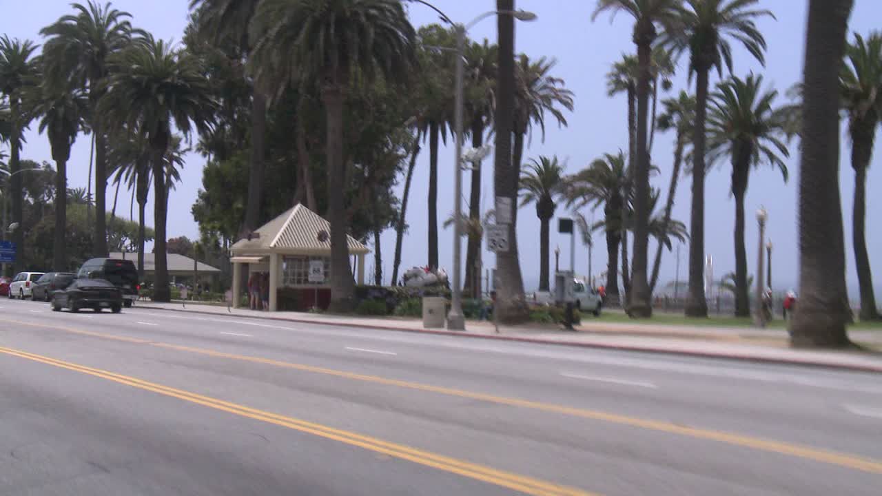 뒤쪽 창문을 통해 비스듬히 보이는 산타모니카 캘리포니아의 해변가를 따라 자동차가 이동합니다.