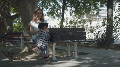 Elegant-middle-aged-woman-sitting-outside,-googling-on-tablet