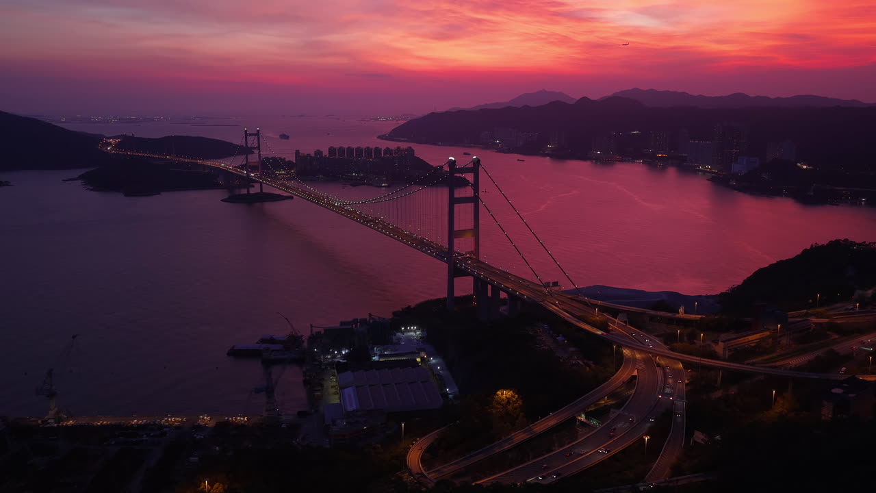 Cinematic aerial view of Tsing Ma Bridge in Hong Kong glowing at sunset, with winding roads, calm waters, and a vivid sky—capturing the essence of scenic travel and urban beauty