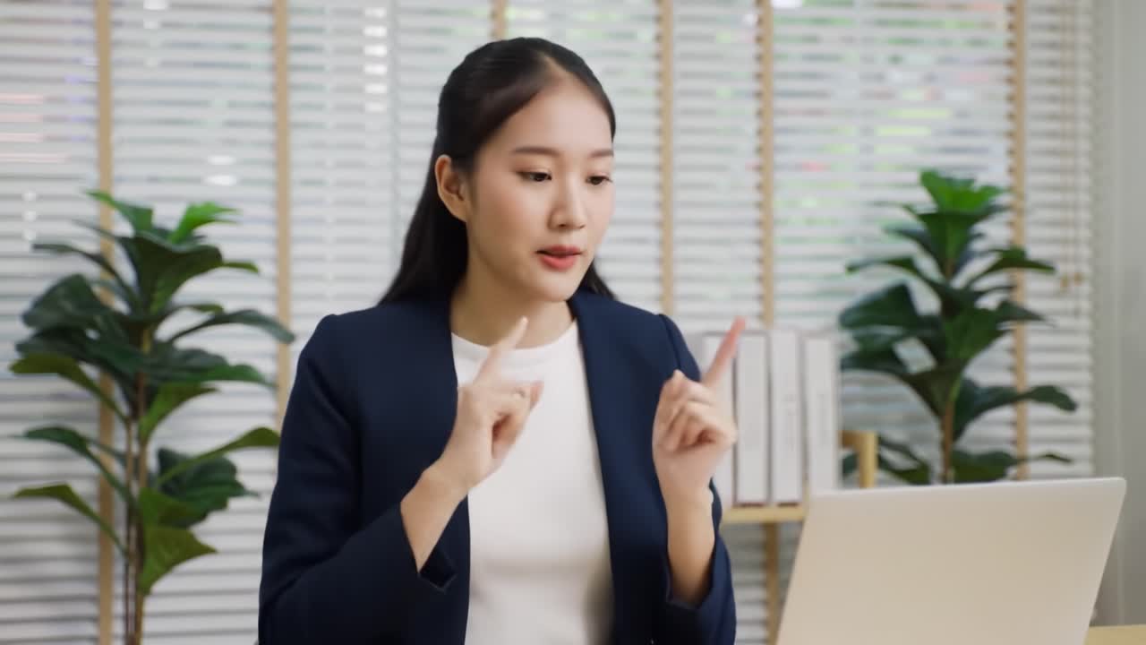 A woman dressed in a professional outfit gestures expressively while participating in a lively virtual meeting within a stylish office environment.