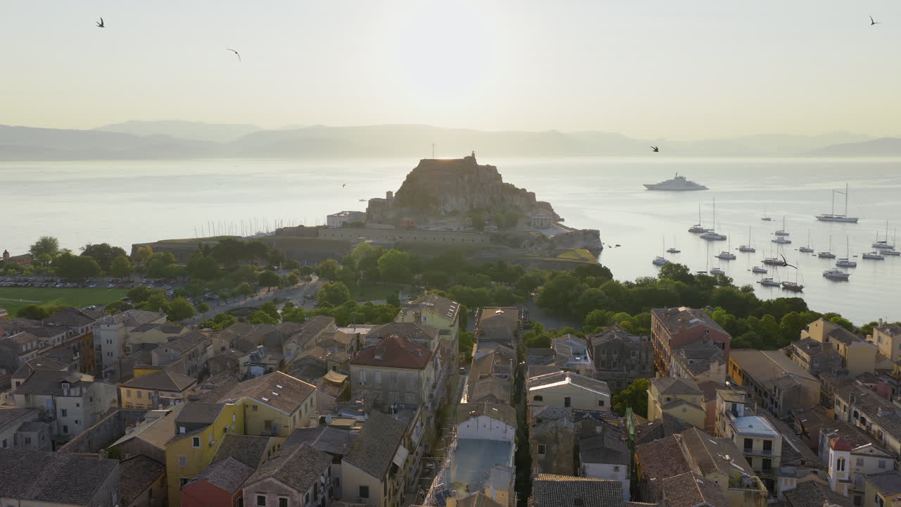 Old Fortress and rooftops of Corfu at sunrise with birds flying in warm morning light, aerial establishing panoramic drone overview
