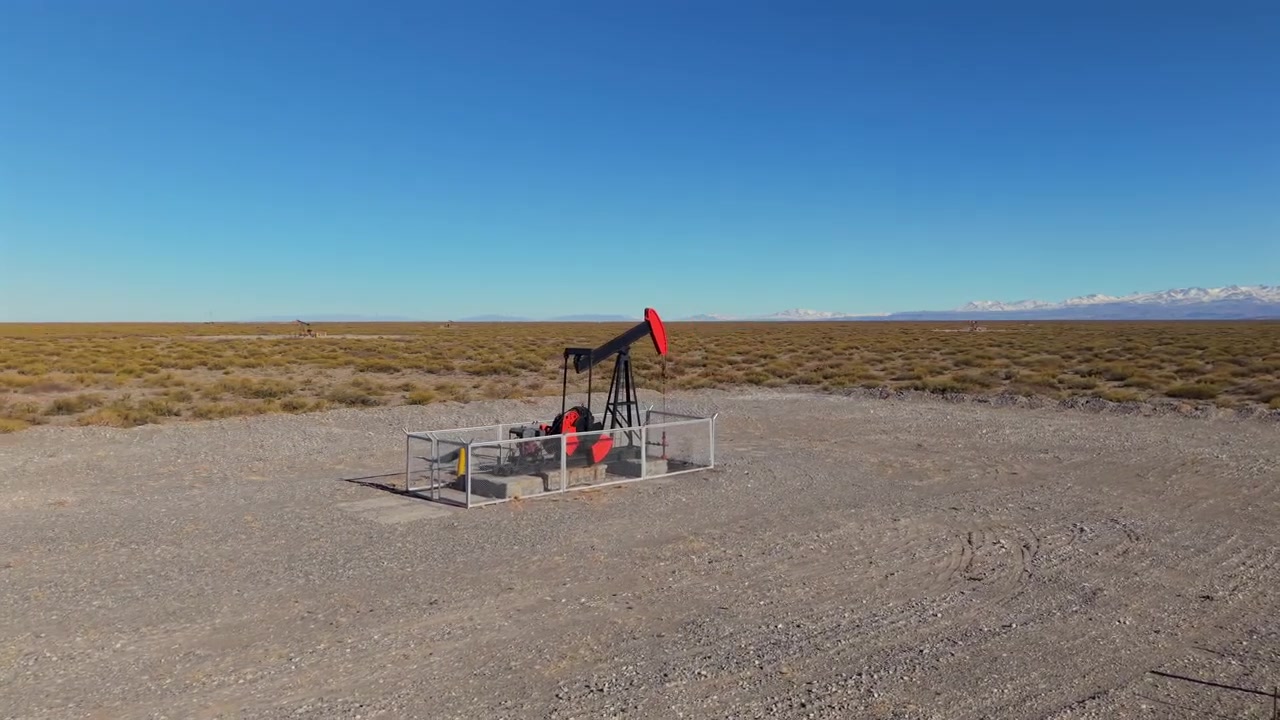 Pompa di estrazione petrolifera in funzione su una pianura arida vicino a Malargüe con lo sfondo delle Ande innevate, orbita aerea media, nessuno.