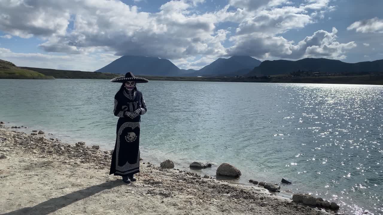 Persona sulla riva del lago travestita da Catrina messicana del Giorno dei Morti che guarda la camera