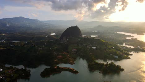 high angle aerial of stone of guatapé above el penol town with vibrant houses and tropical lake, surrounded by mountains
