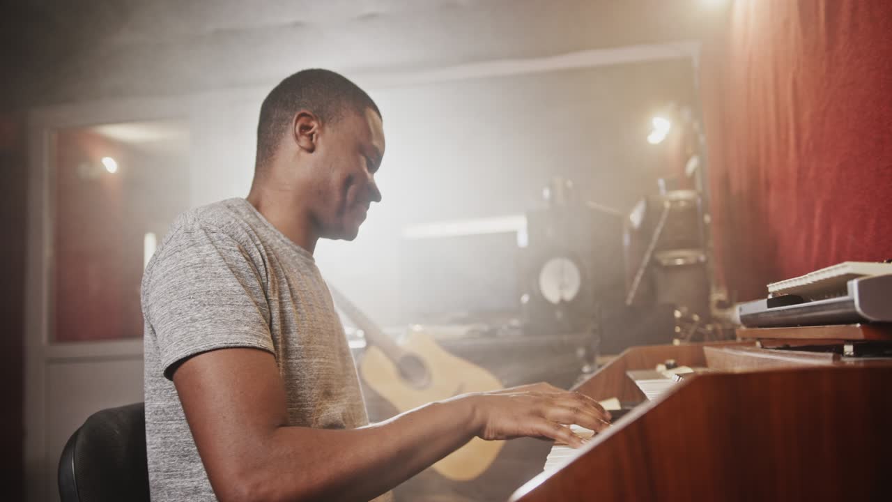 Black man playing synthesizer in recording studio